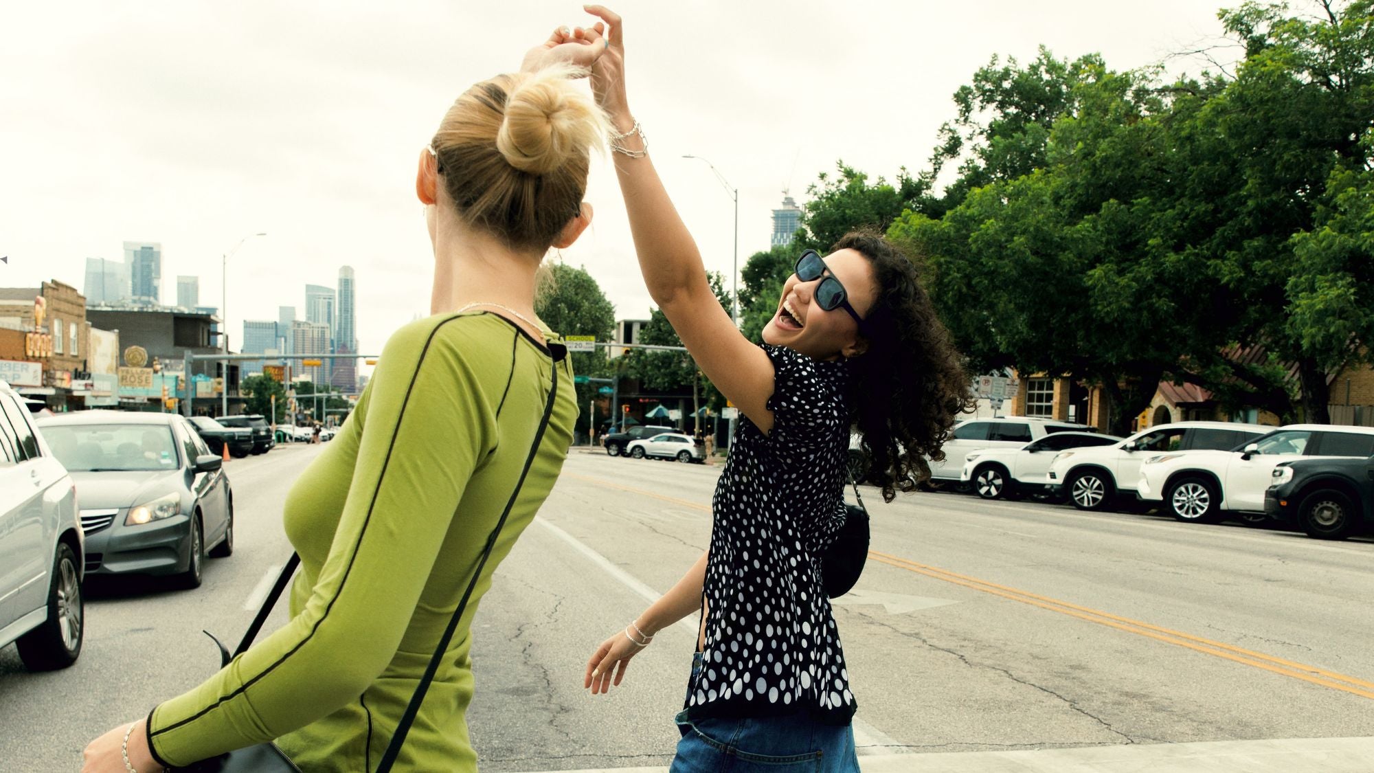 Two women high-fiving on a city street with buildings and cars in the background.