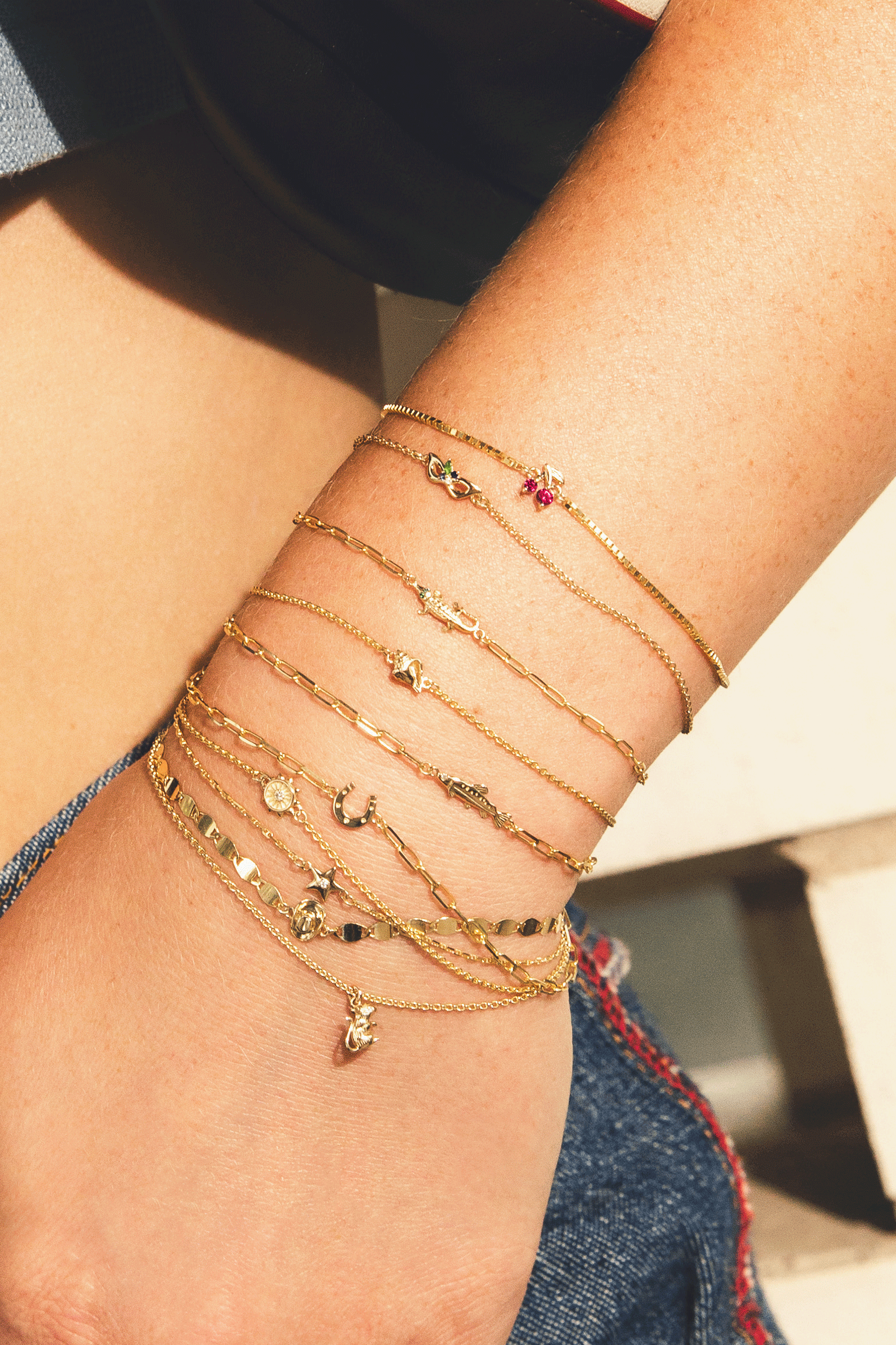 Close-up of a wrist wearing multiple gold bracelets with various charms.